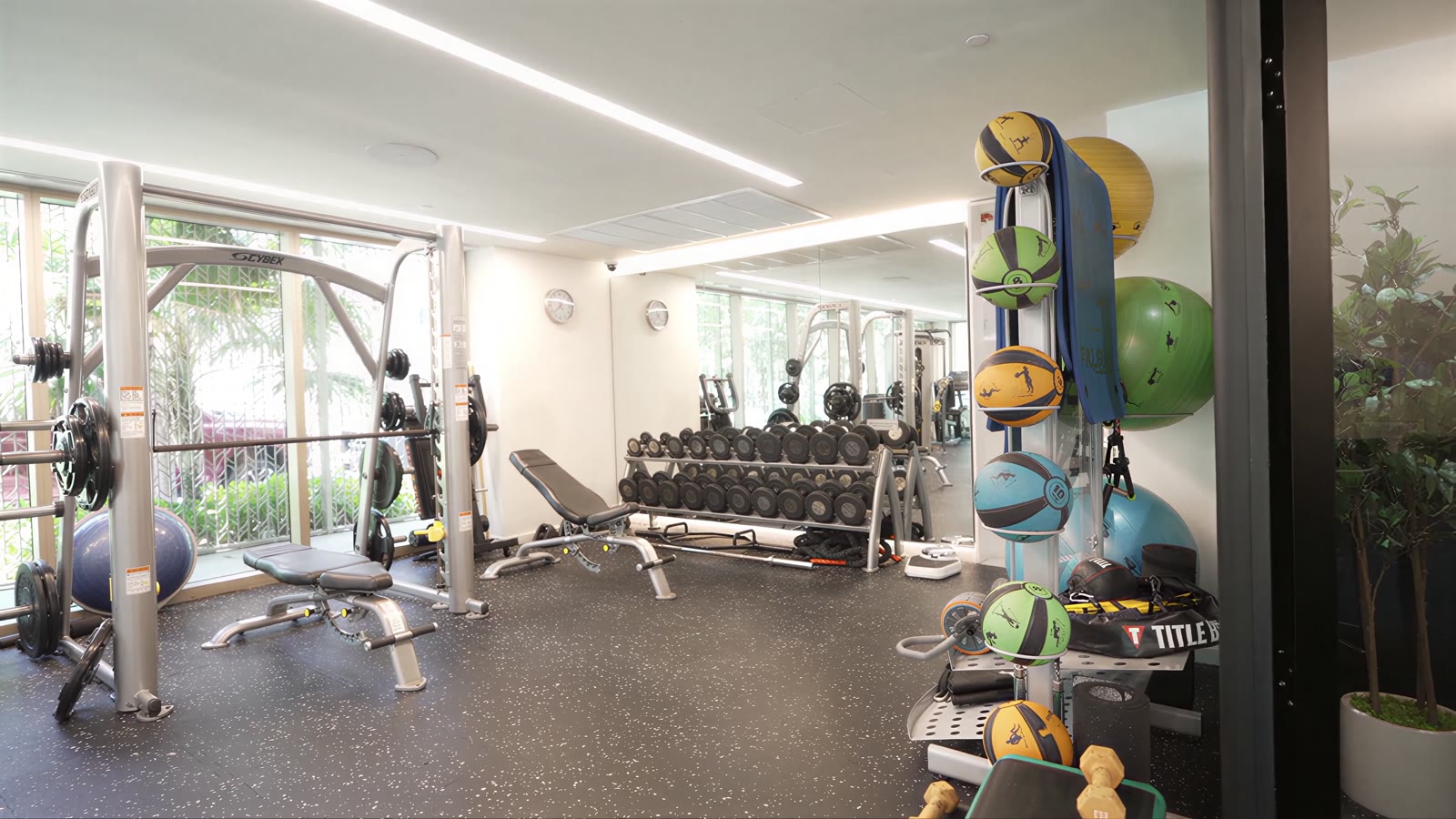 The fitness center at 300 Collins before the work, with weight racks, benches and floor-to-ceiling windows.
