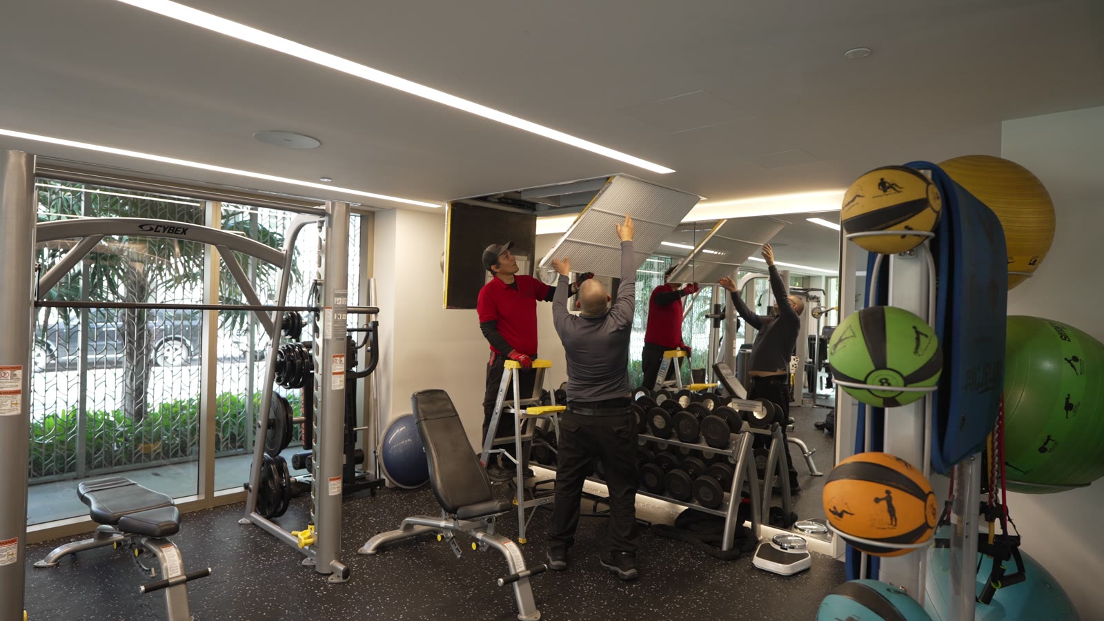 ABC Mechanical technicians in red shirts lifting a ceiling panel out of the way on a ladder inside the fitness center during Day 1 of the tear-out.